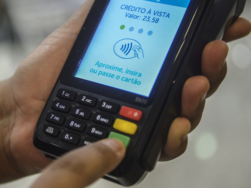 Foto de uma máquina de cartão de débito e crédito. Na tela, está escrito: 